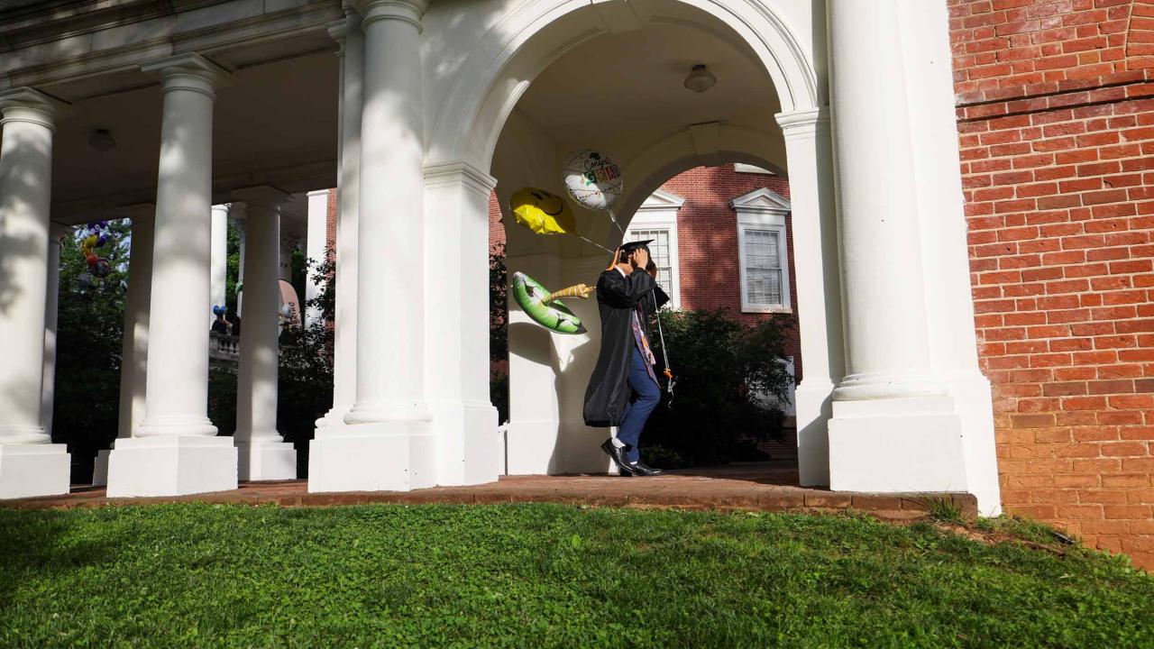 A graduate adjusts their mortarboard as they walk over to the Rotunda to line up for Final Exercises 2025