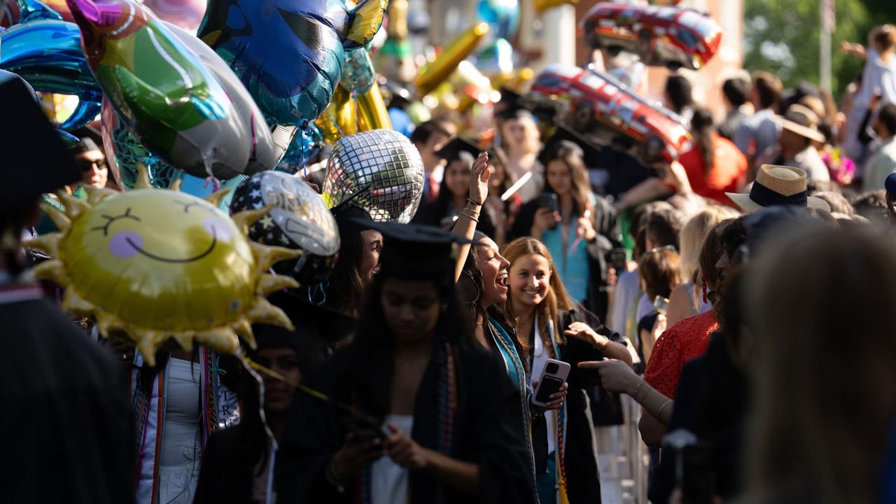A 2025 graduate pauses in the procession to give a joyful smile and wave to their family