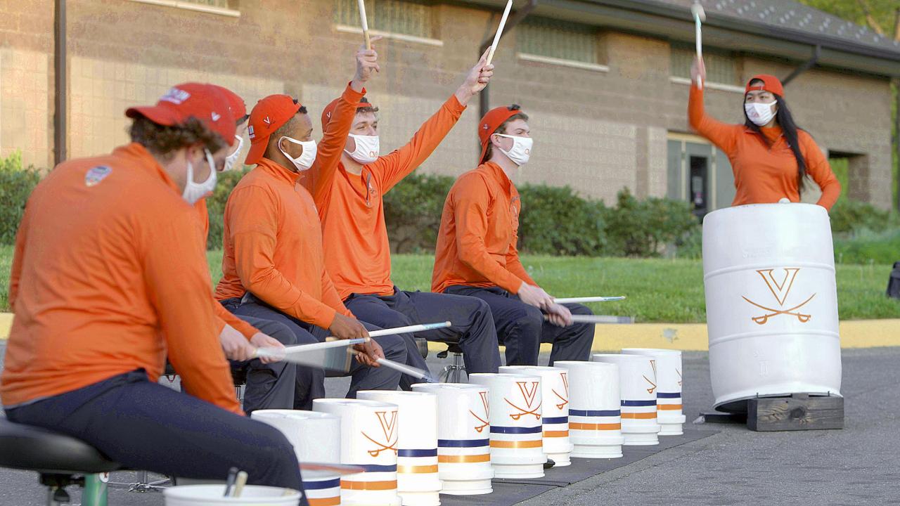 Percussionists drumming on UVA branded buckets while one member has both drumsticks in the air 