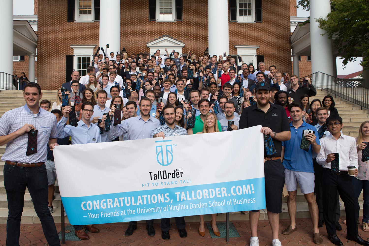 Dan Friedman left, and  Mike, holding the sign that says Congratulations, Tallorder.com! a group of fellow students stand behind them on steps