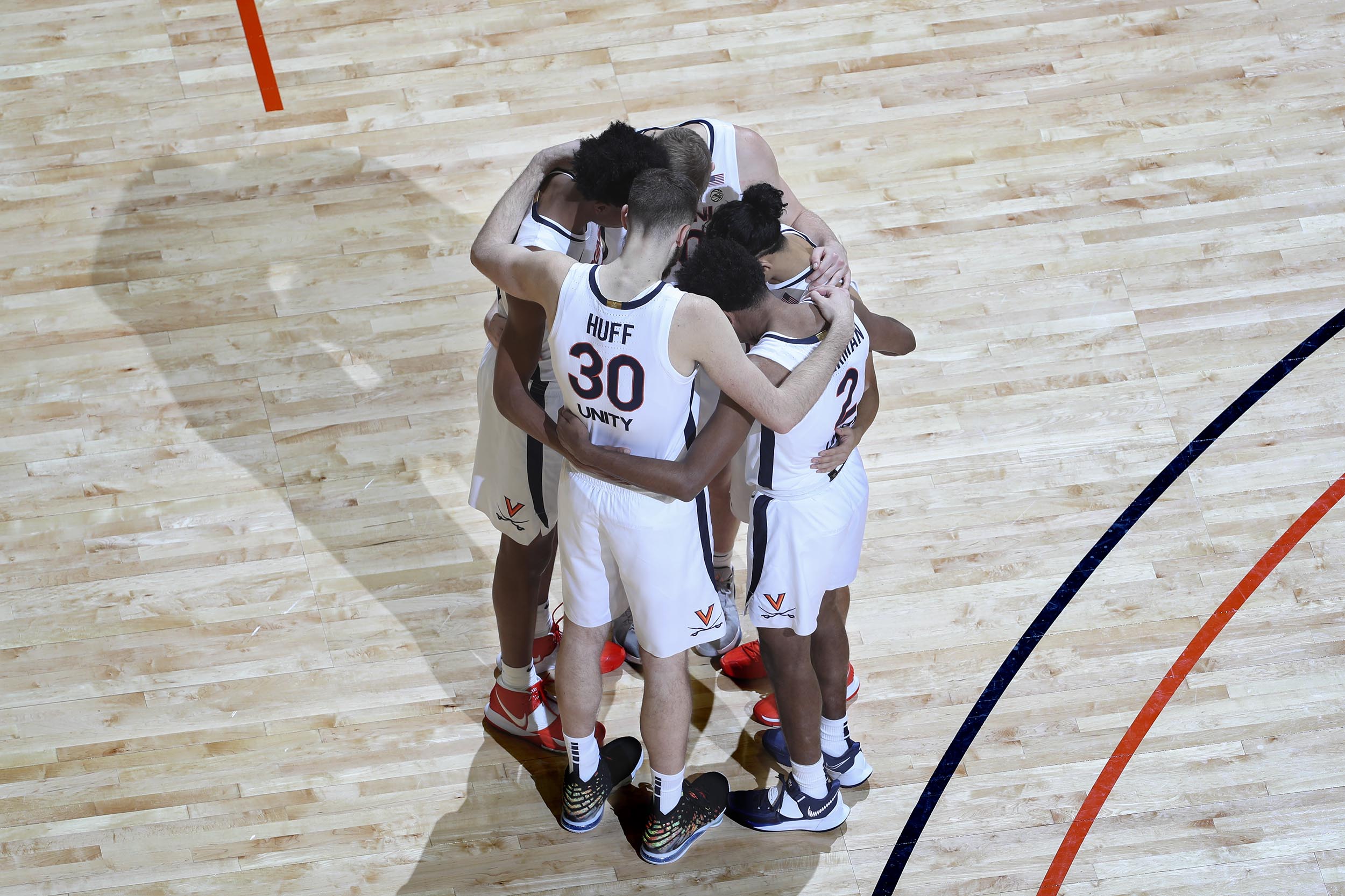 5 UVA basketball teammates huddle together on the court with their heads together