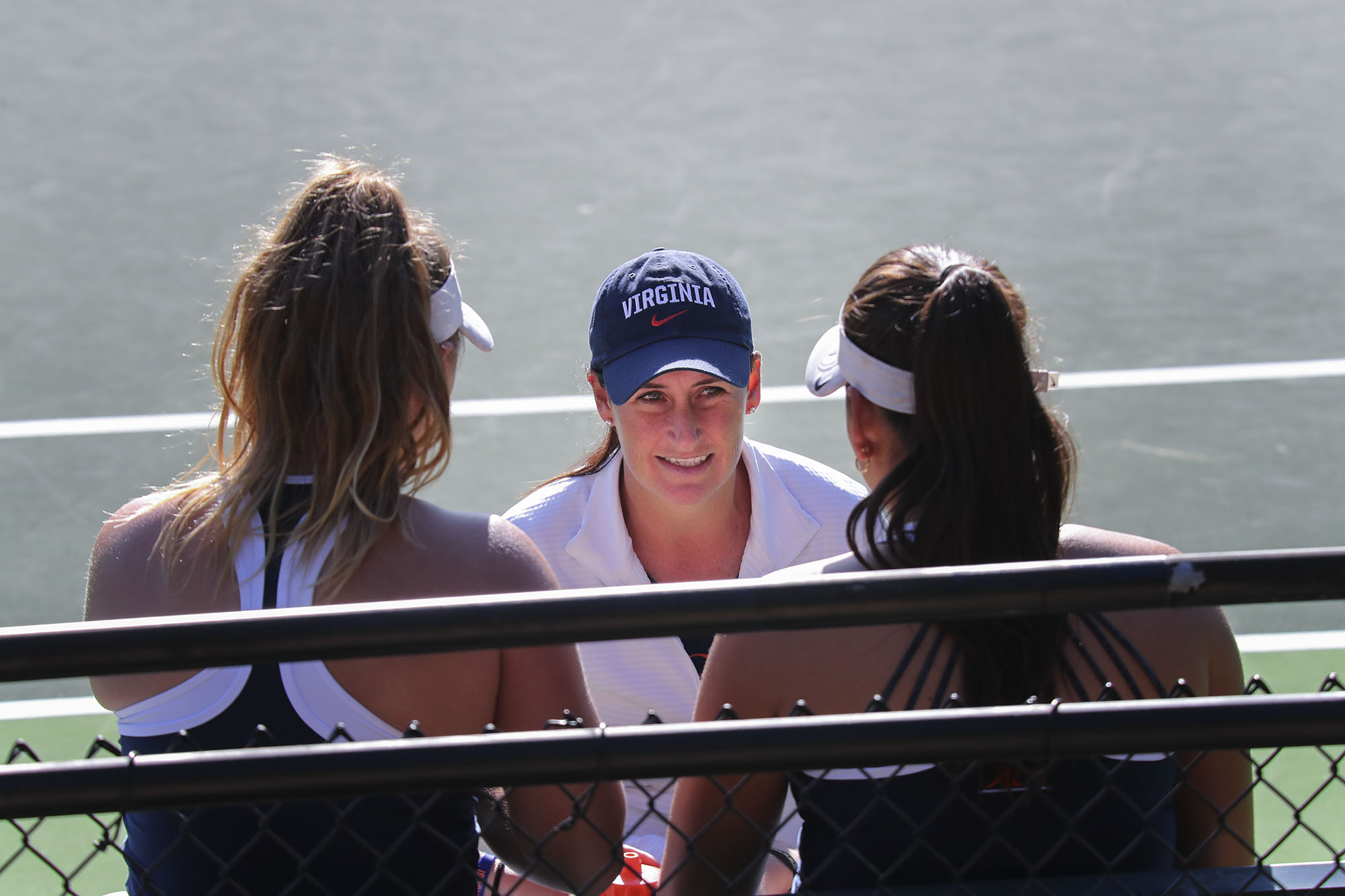 Tennis coach talking to two female tennis players who are sitting on a bench