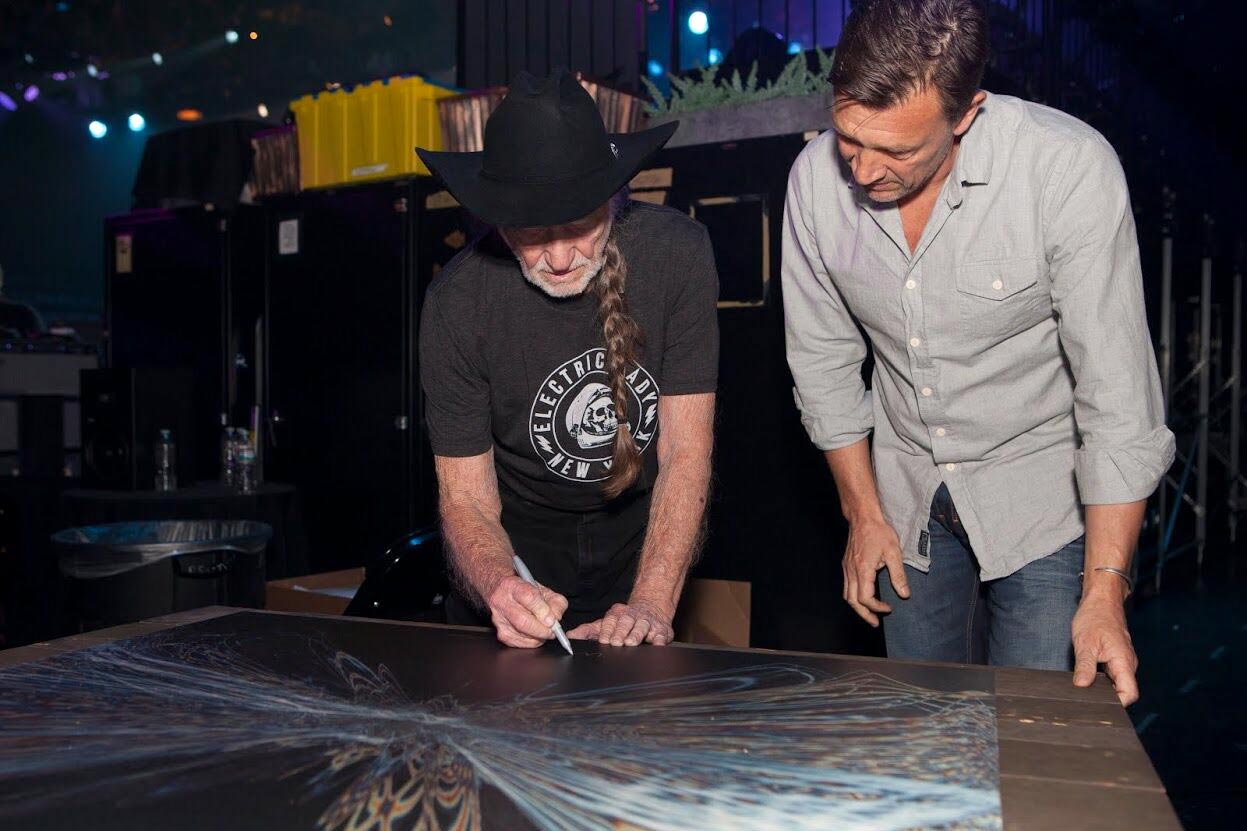 Tim Wakefield, watches Willie Nelson, left, sign a piece of art