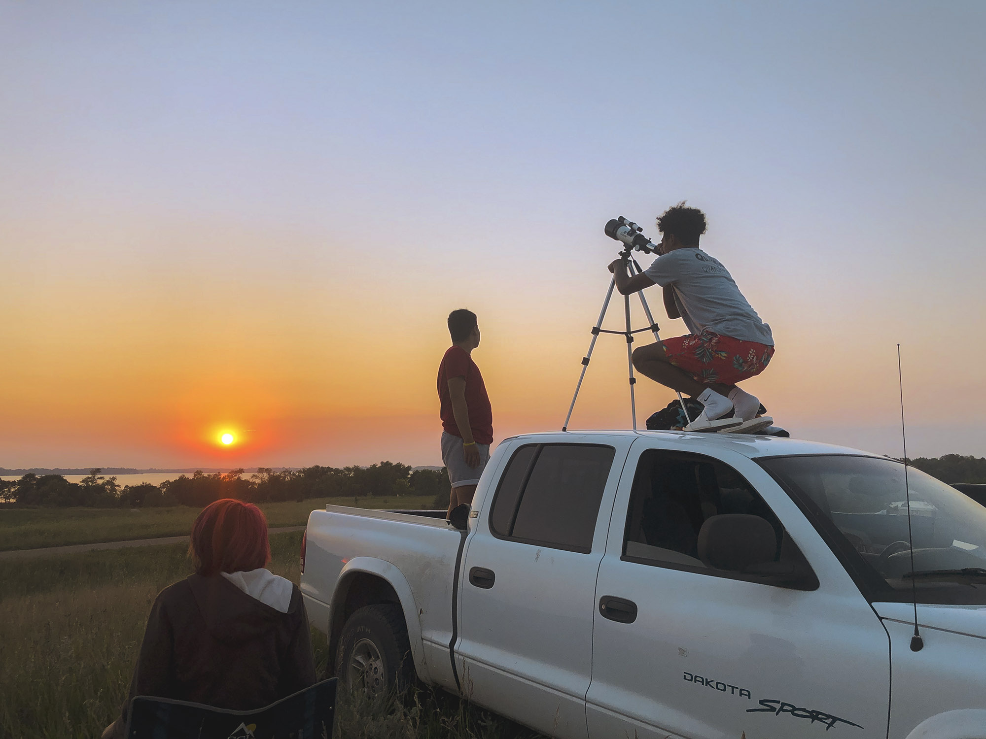 People on top of a white dodge Dakota looking at the stars through a telescope