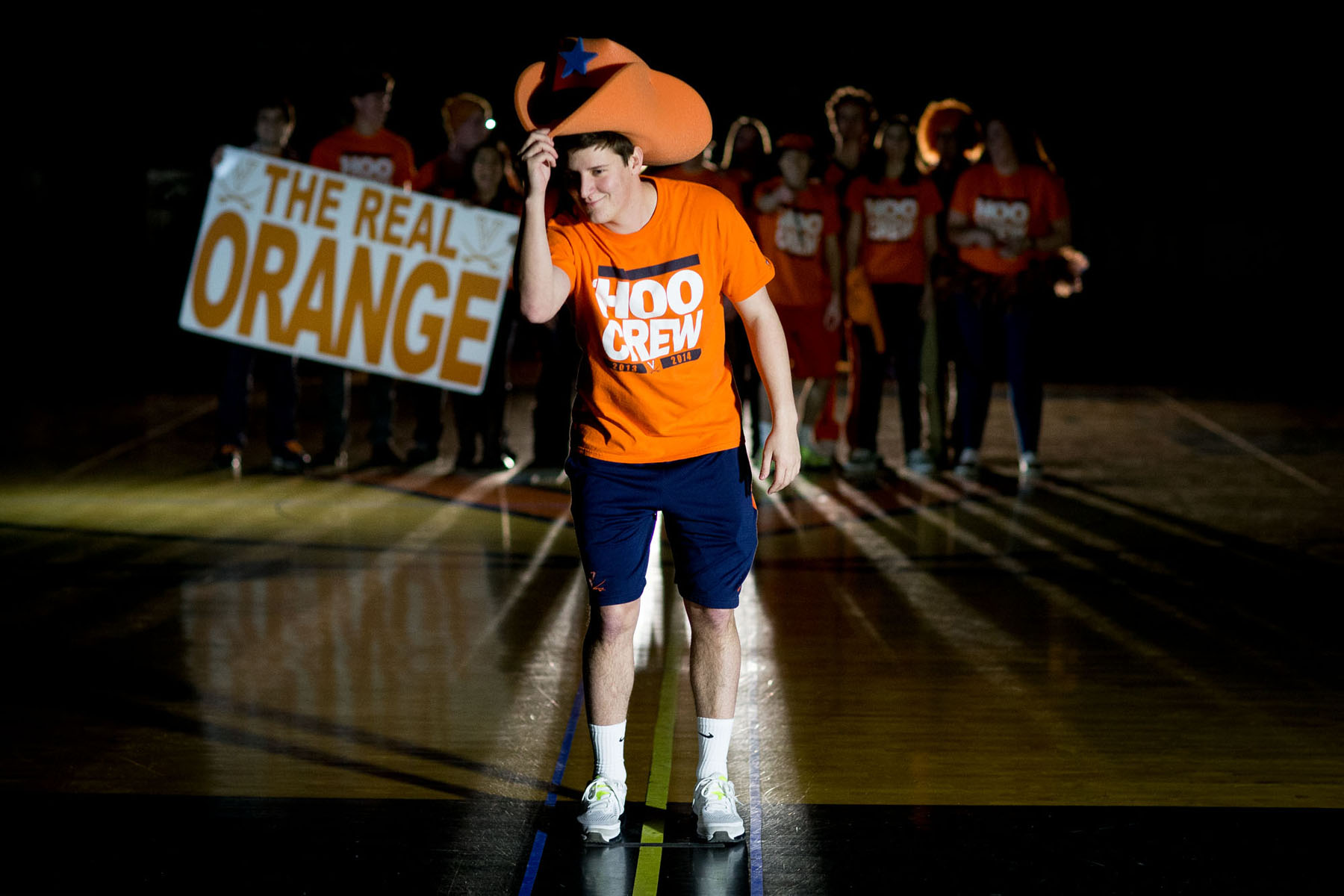 Man standing in front of a group of students all dressed in UVA gear tilting a big orange hat towards the camera