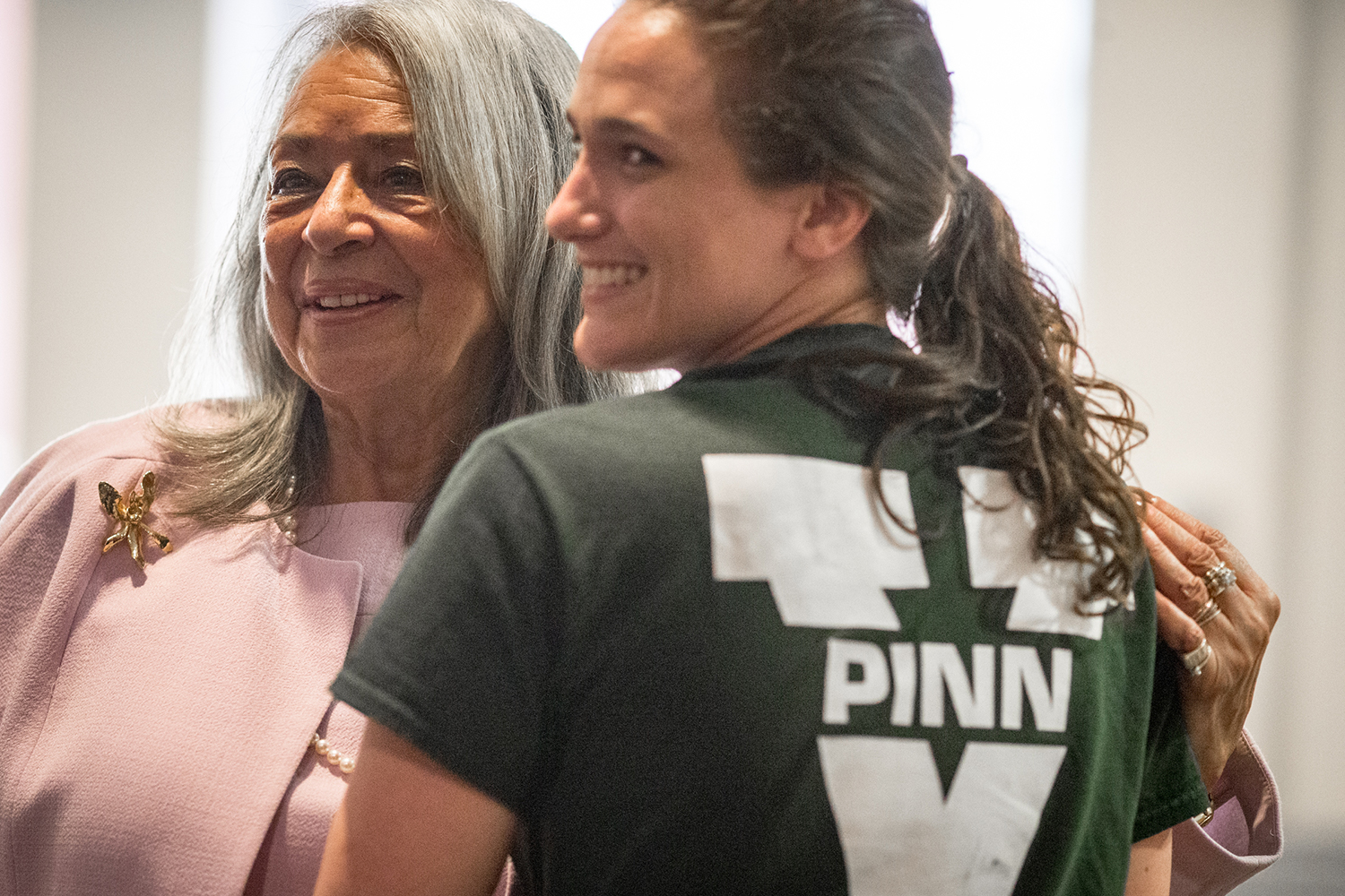 Two women stand together.  One has a shirt that has a UVA V with the word PINN in the middle