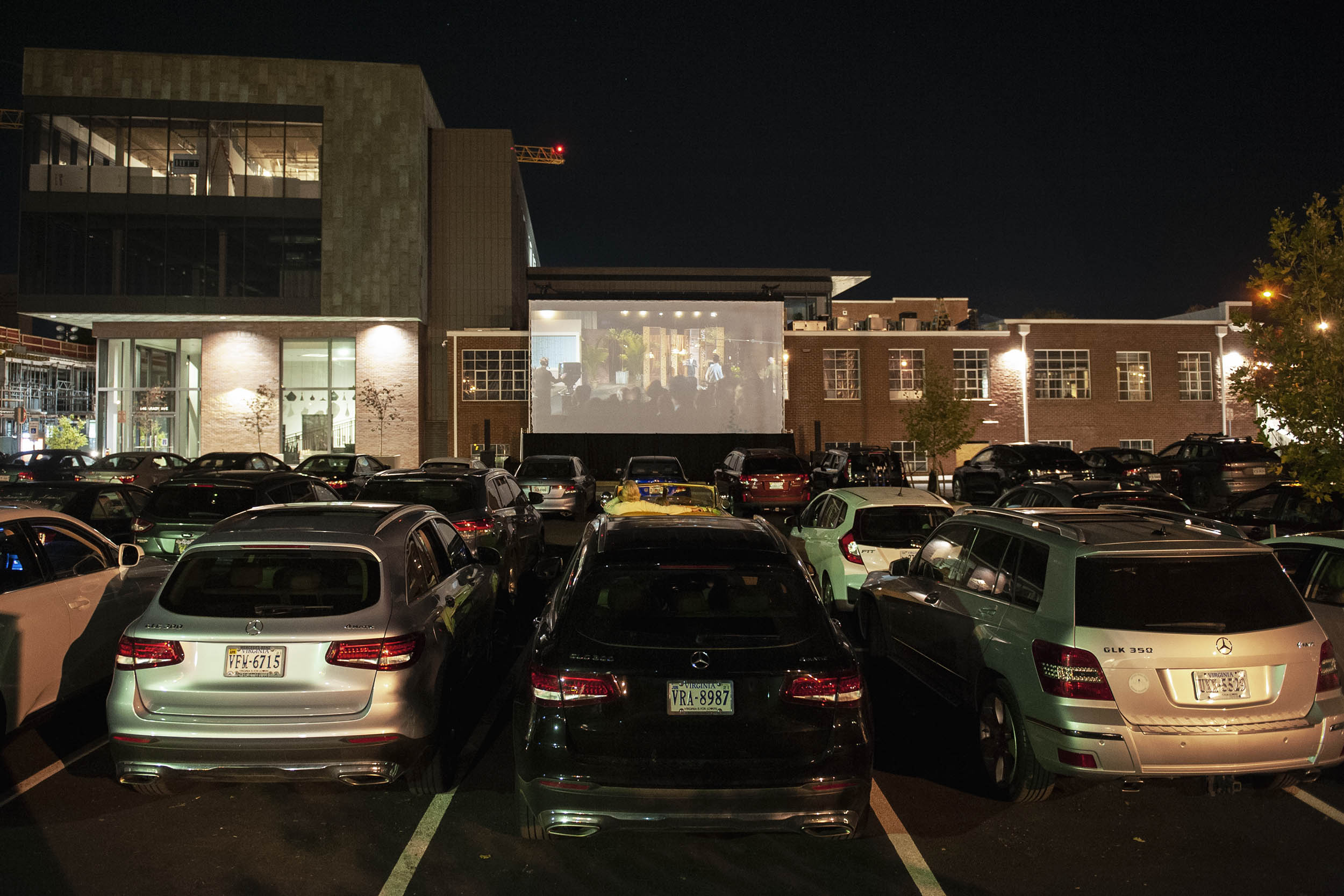 Cars in parking lot watching a movie on a screen outside of a building