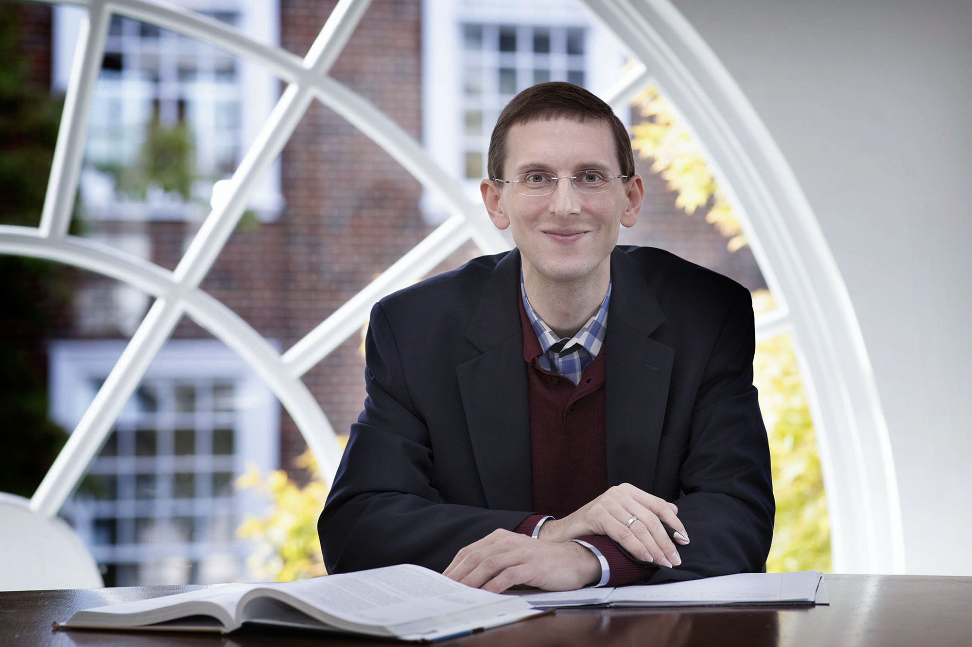 Anton Korinek sits at a table with books open looking at the camera