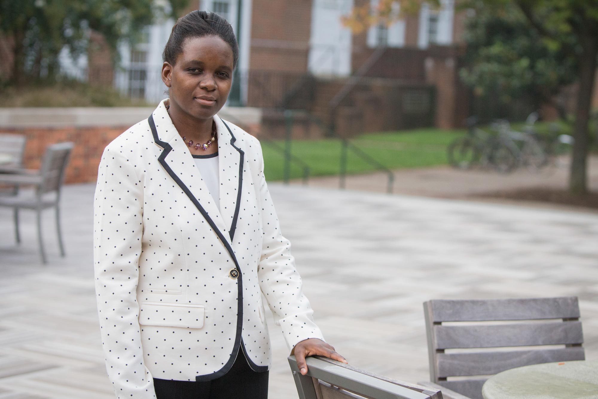 Vivien Chabalengula standing looking at the camera with one hand holding an outdoor chair