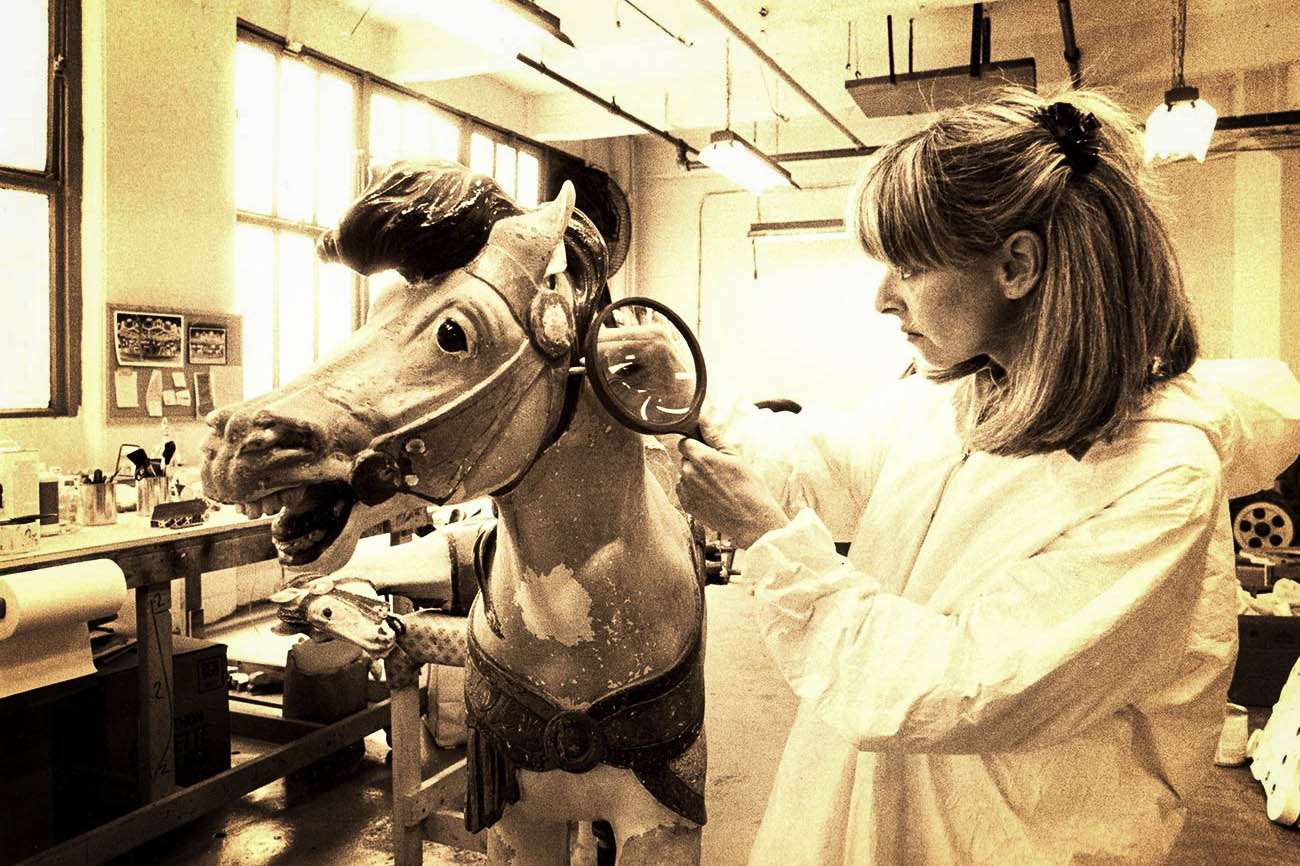 Jane Walentas holding magnifying glass as she restores a carousel horse