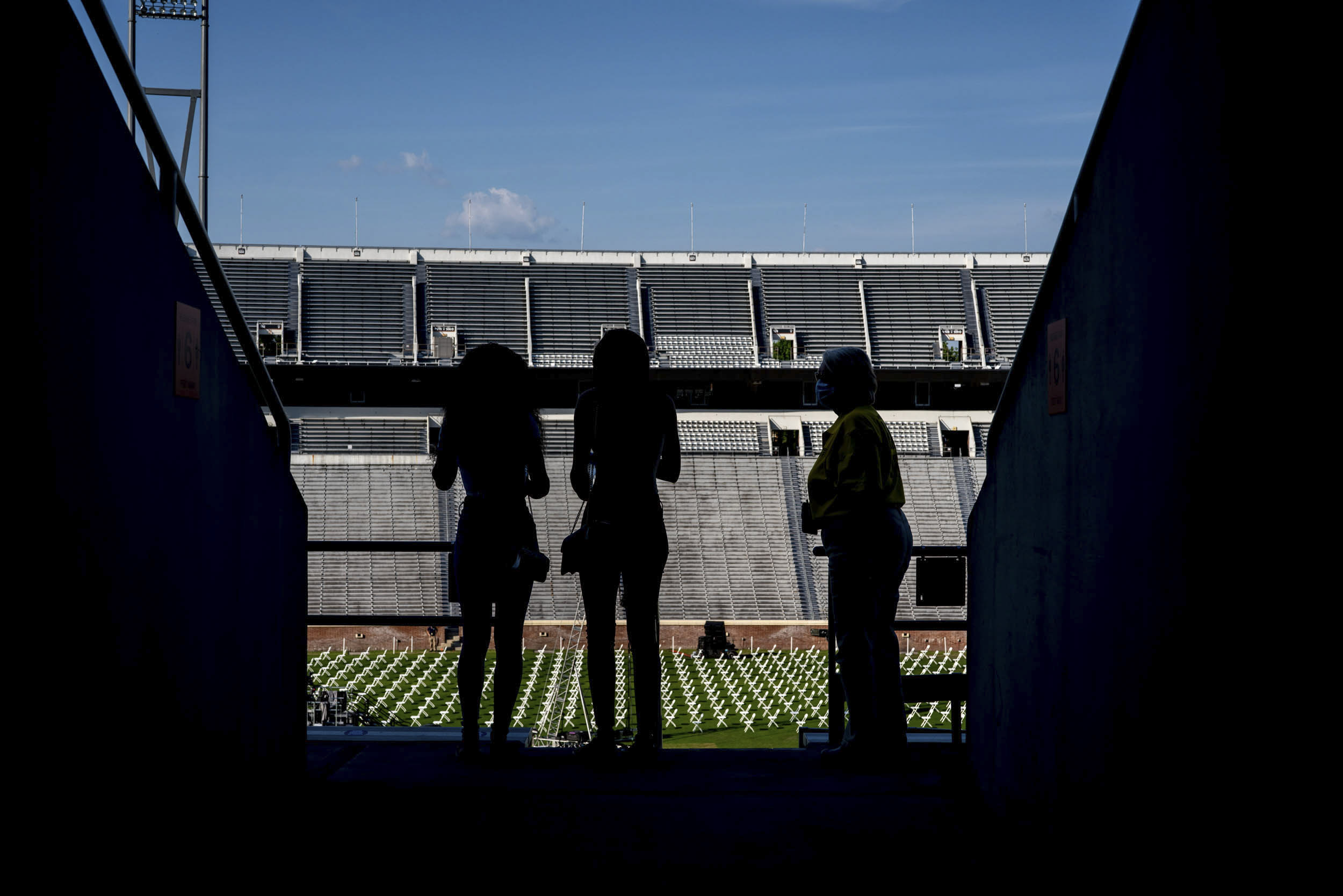 Silhouettes of three people looking on the field of empty graduate chairs