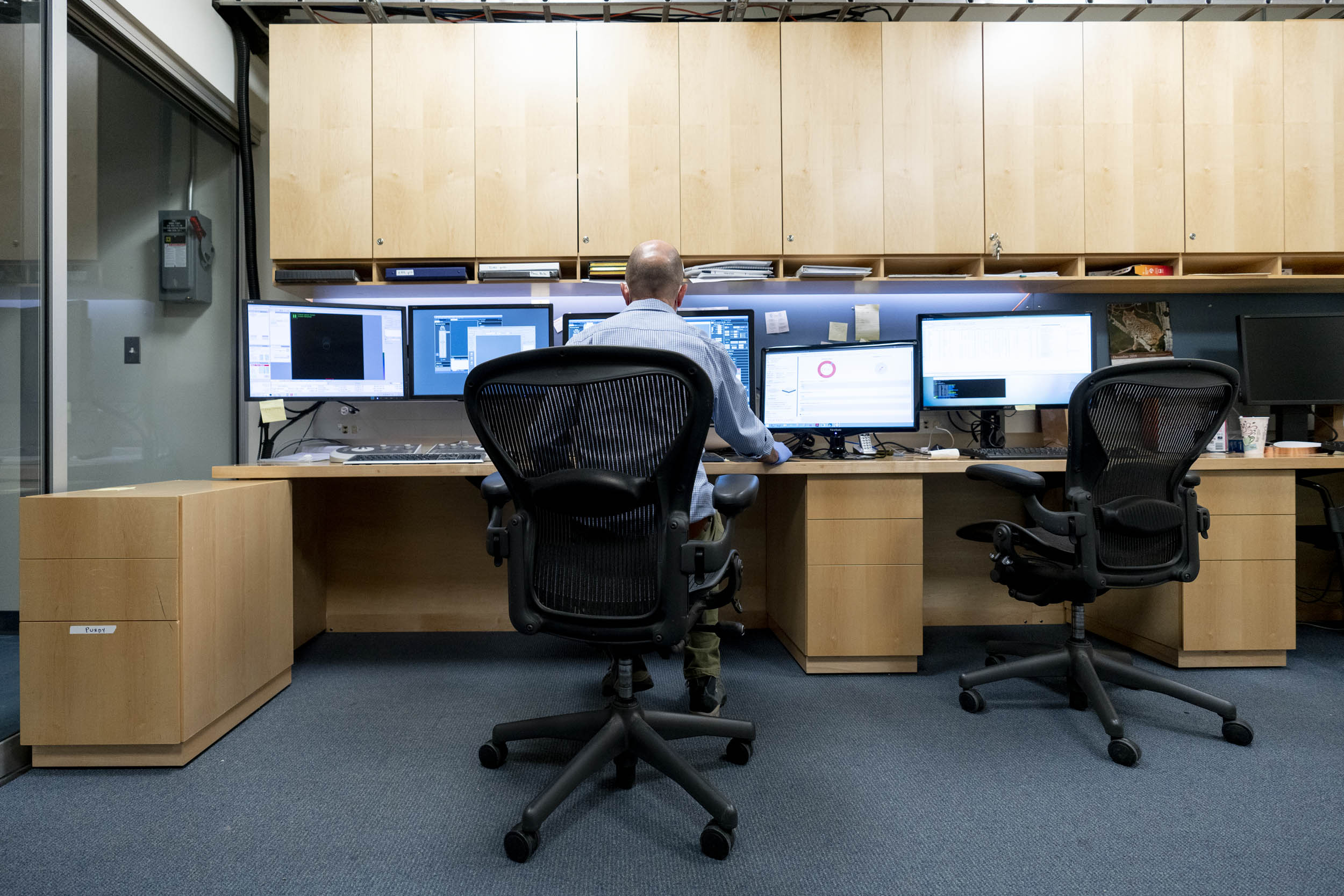 Man sitting at a desk looking at 5 monitors