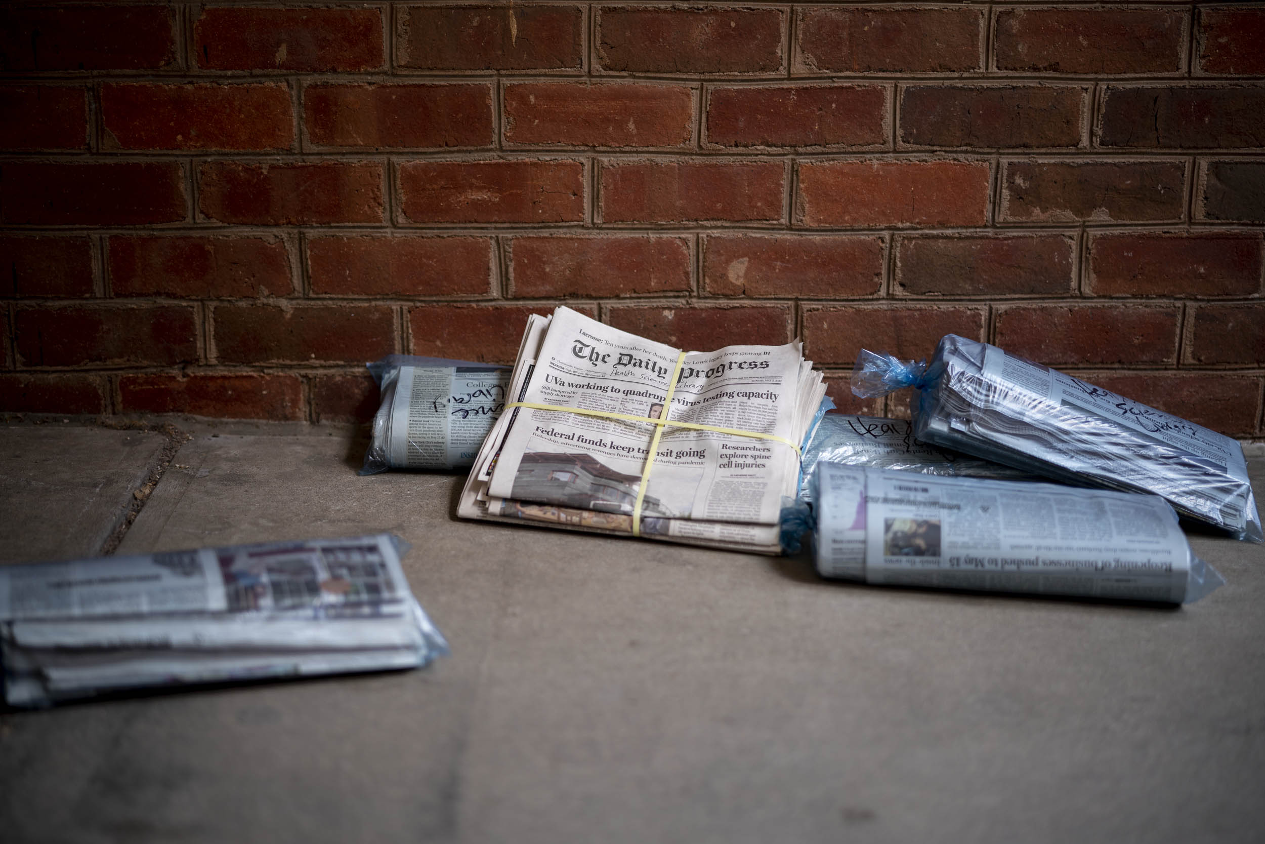 Stack of uncollected Newspapers on a sidewalk next to a brick wall