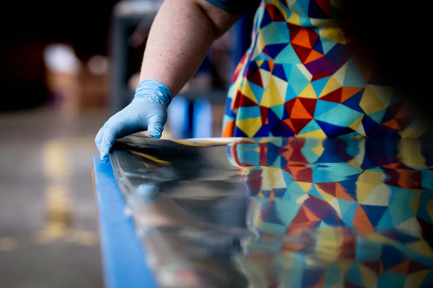 Person standing next to a table wearing blue gloves while stacks of plastic sheets are in piles on the table