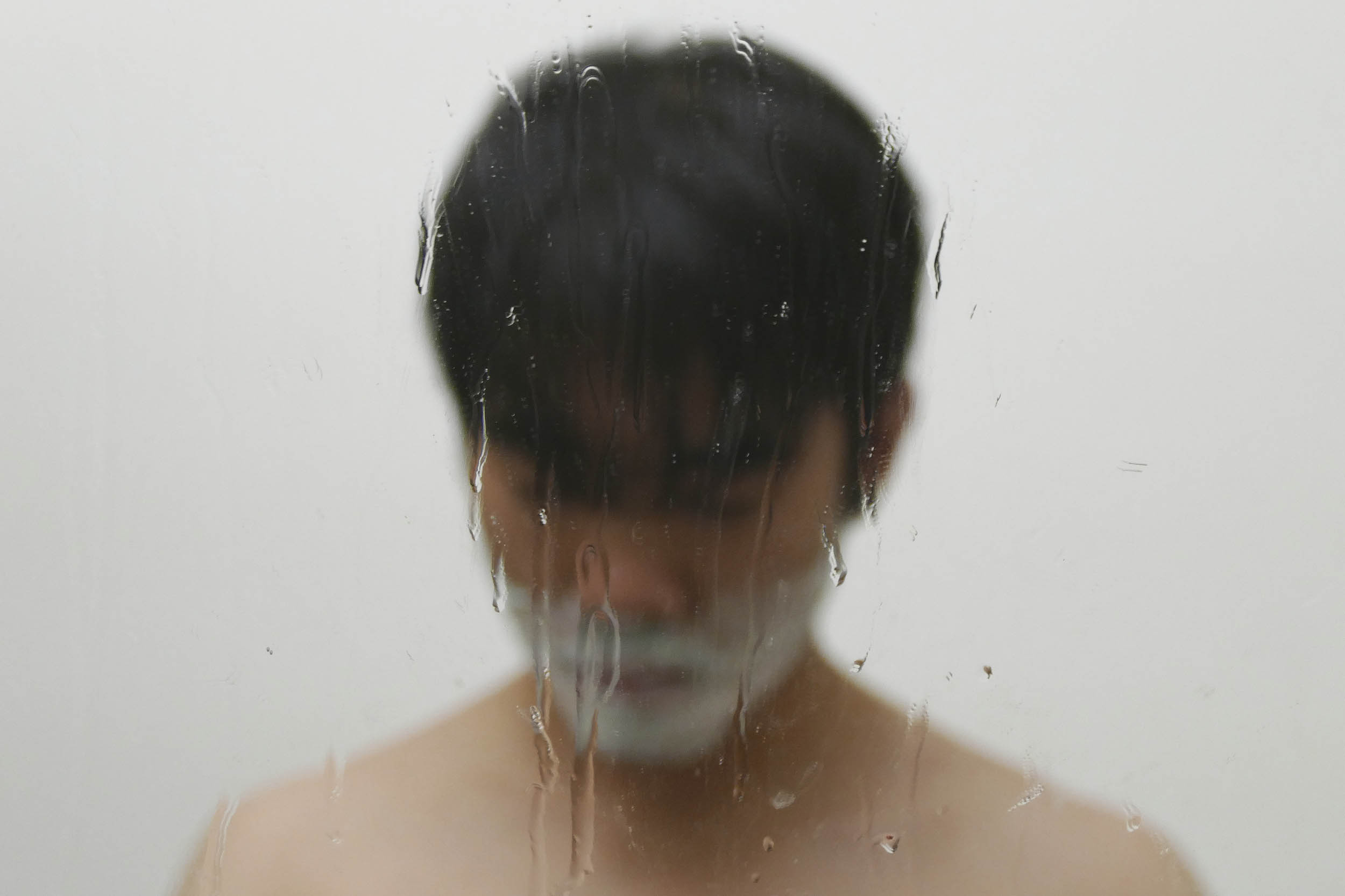 Winston Tang shaving in a mirror with water running down the mirror