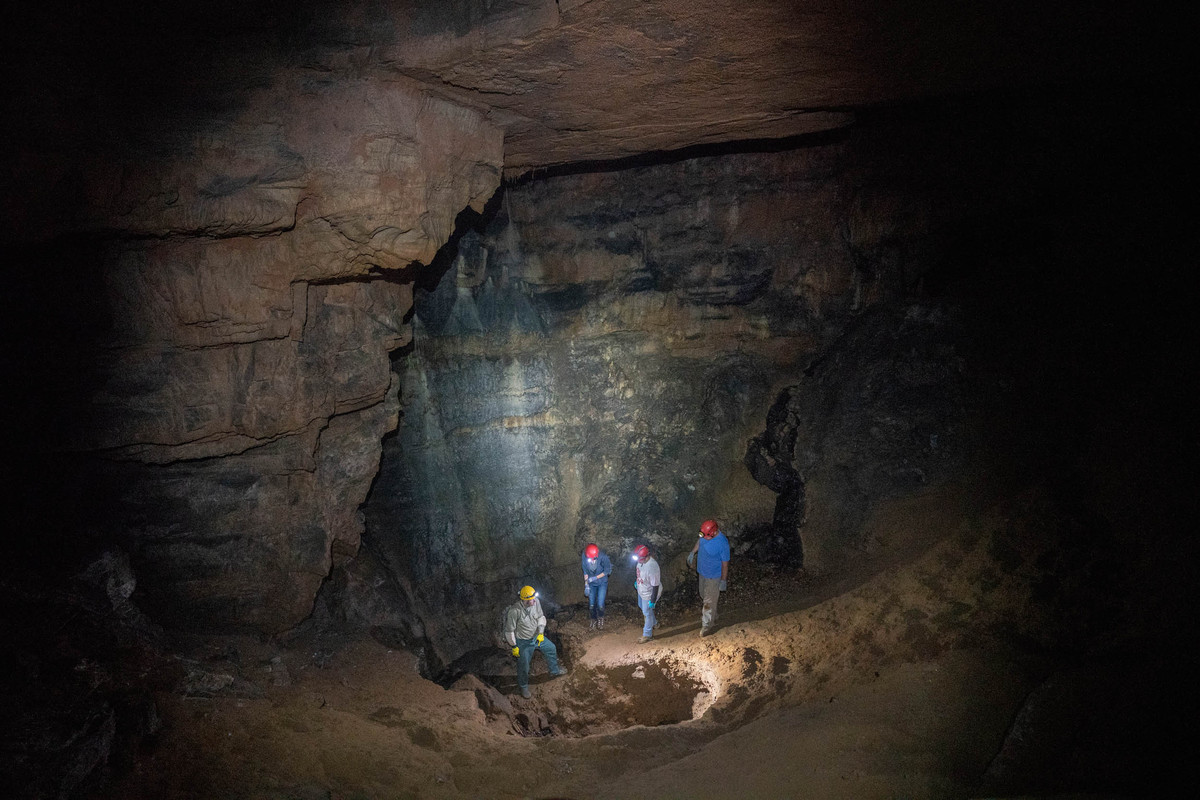 Four people in a cave looking into a big hole