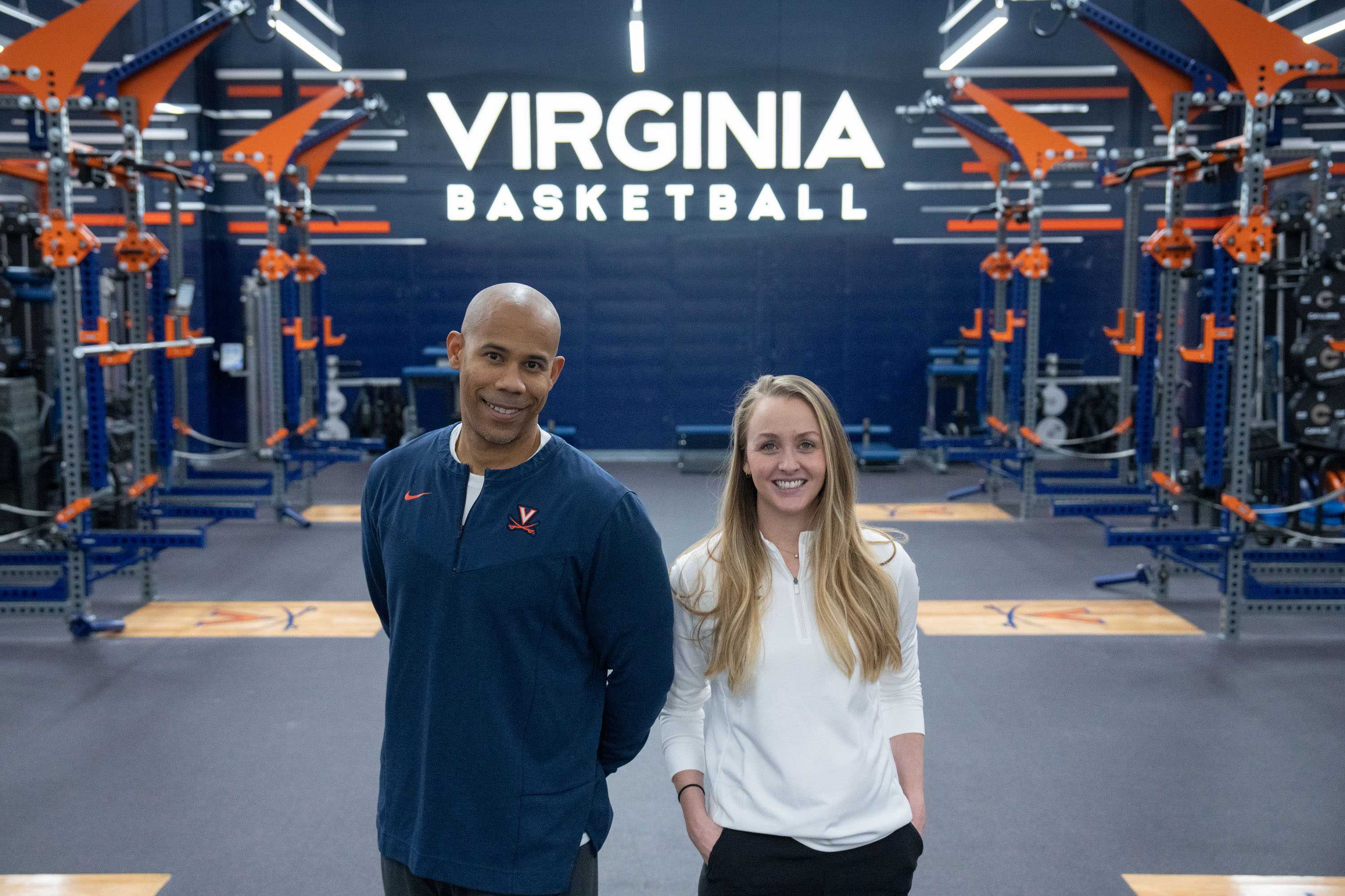 Mike Curtis and Natalie Kupperman standing in the middle of the weight room looking at the camera, smiling